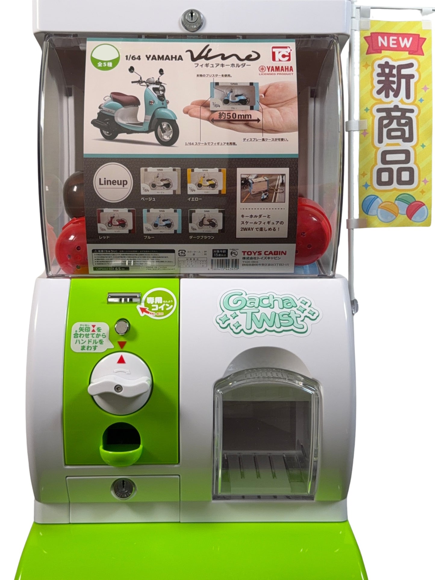 A Japanese toy gacha cabinet machine, featuring a white and lime green body, a clear display window showing a Yamaha Vespa toy, and a vertical yellow banner on the right with Japanese text.