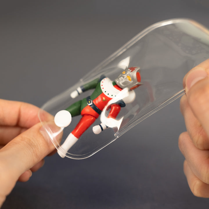Hands stretching the clear miniature package containing the Eisenborg sofubi mascot