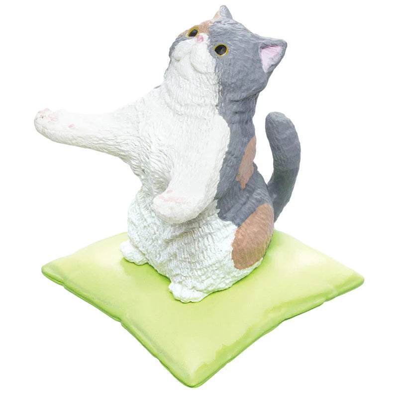 A figurine of a gray, white, and brown calico cat sitting on a light green square cushion, set against a plain white background.