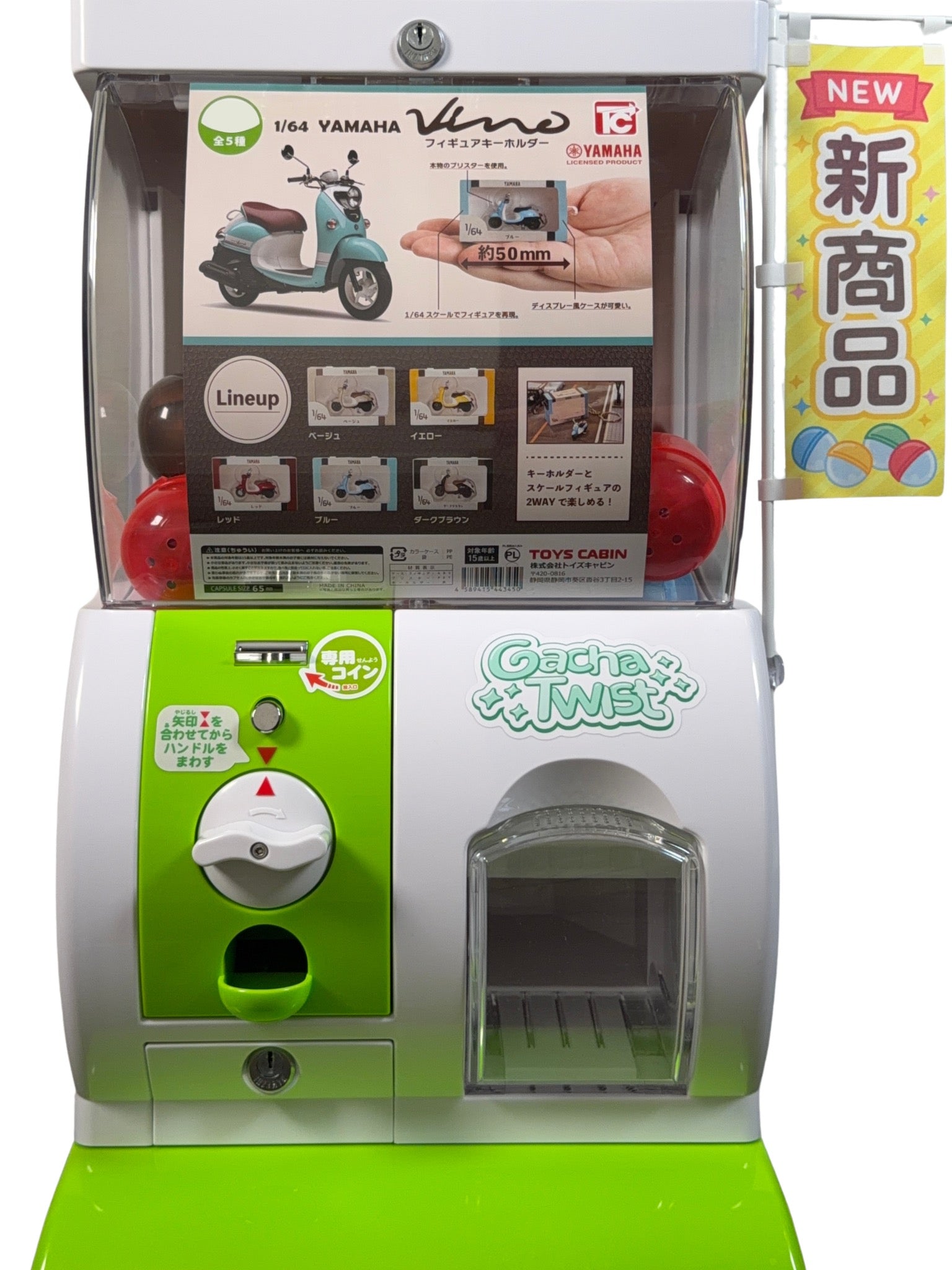 A Japanese toy gacha cabinet machine, featuring a white and lime green body, a clear display window showing a Yamaha Vespa toy, and a vertical yellow banner on the right with Japanese text.