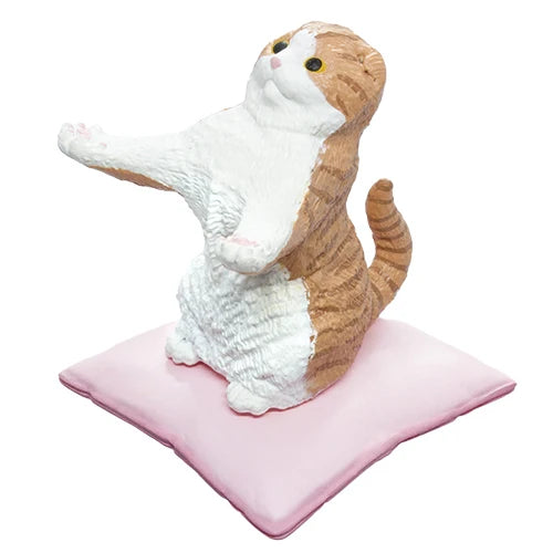 A  cat figurine sitting on a pink cushion, designed to look like a stretching orange and white tabby cat.