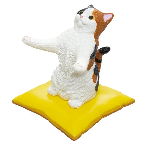 A small figurine of a calico cat sitting on a yellow square base, photographed against a plain white background.