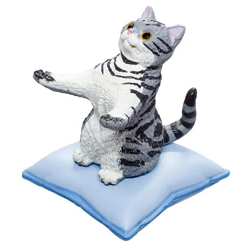 A gray and white tabby cat figurine sitting upright on a light blue cushion, photographed against a plain white background.